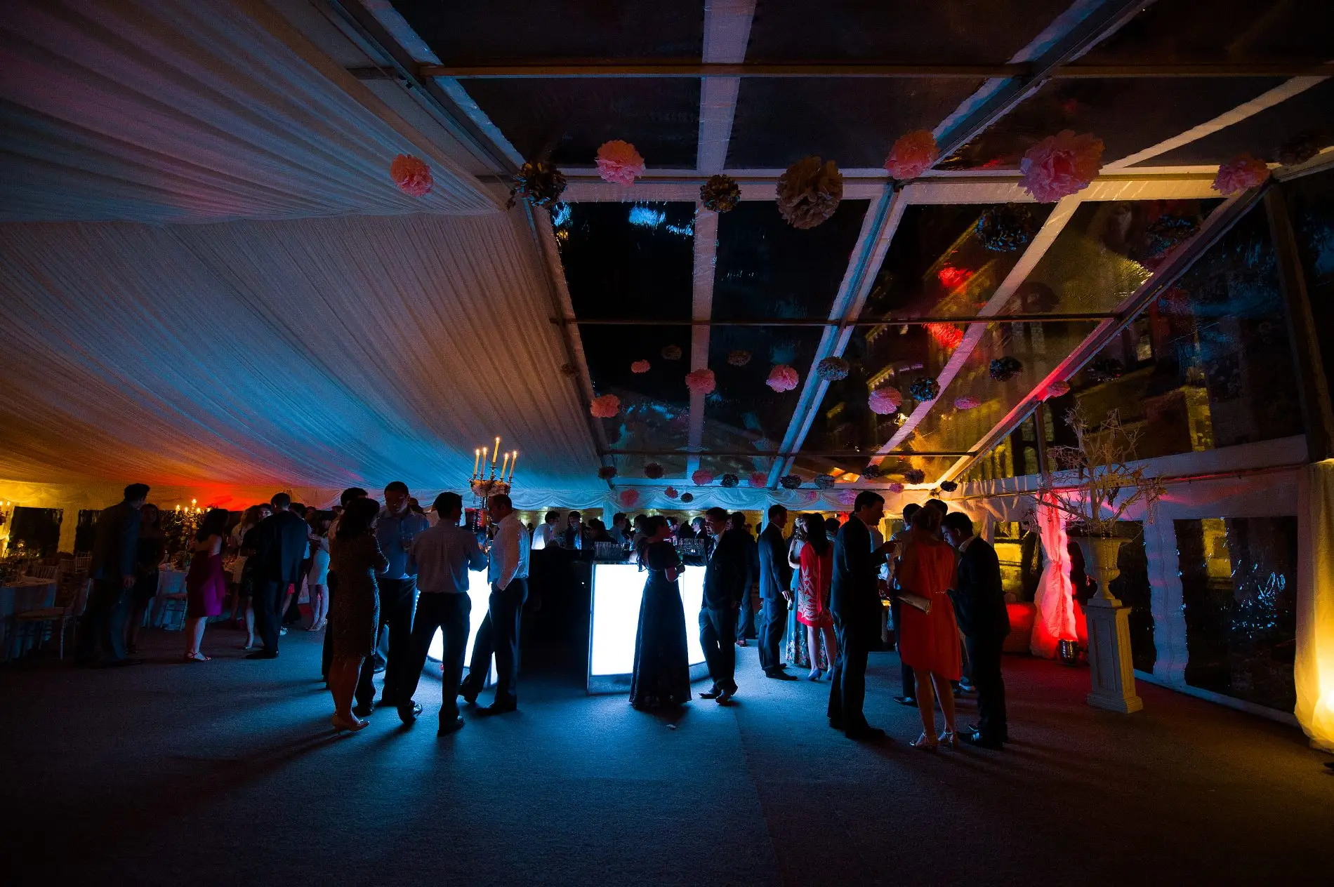 People gathered around a lit bar inside a marquee with drapes at a festival event